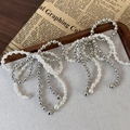 Schoenbedeltje in strikvorm met witte parels en zilveren kralen op vintage krant - Wit & Zilver