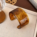Close-up of amber resin bangle showing marble texture on a textured beige tray - Amber Wide Edge (25722E)