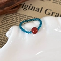 Close-up of mint green beaded ring with a bold red statement bead on a shell tray - Red Bead Style (25765B) / Dark Blue and Red