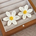 Close-up of woven raffia daisy earrings in white and yellow on a wooden jewelry display - White Daisy Style (25585A)
