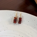 Macro shot of gold hook earrings with red-brown beads on white ceramic plate - Red Agate Style (24356B)