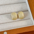 Detalle de pendientes geométricos de oro mate con textura brillante en un joyero de lujo - Estilo de Frijol Dorado Brillante Esmerilado / Dorado