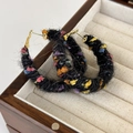 Detail view of colorful mixed-weave plush hoop earring on a wooden jewelry display - Black Multi-color