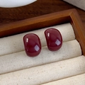 Macro view of dark red bean-shaped stud earrings with glossy enamel glaze on beige display - Minimalist Bean Style (21# 26105A)