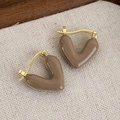 Dettaglio di orecchini a cuore in smalto marrone caffè su tessuto beige minimalista - Orecchini a Cuore in Smalto Semplice (24068A)