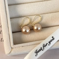 Primer plano de pendientes de perlas champagne con ganchos dorados en caja beige - Perla Artificial Champaña (10mm)
