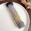 Close-up of multicolored elastic hair ties in a transparent storage tube with textures - Gray Colorful