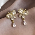 Elegante goldene Schmetterlingsohrringe mit funkelnden Kristallen auf rosa Seidenhintergrund - Gold Schmetterling Stil