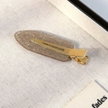 Detail der champagnerfarbenen Glitzer-Haarklammer mit goldener Metallbasis auf Stoff - Beige