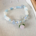 Detailed shot of beaded bracelet with pink peach charm, blue flowers, and white beads - Blue