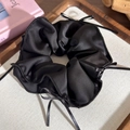 Dettaglio di un elastico in raso nero con eleganti fiocchi su un vassoio di legno - Nero