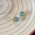 Detailansicht quadratischer Gold-Ohrstecker mit blauer Perle auf einem Keramiktablett - Gelee-Blau