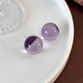 Makro-Detail von transparenten lila Harzkugel-Ohrringen auf weißem Keramiktablett - Amethyst