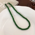 Close-up of emerald green beaded necklace with silver buckle on a white textured plate - 6mm / 6mm Necklace