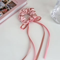 Detailed macro view of pink silk satin scrunchie with long ribbon bow on white desk - Small / Pink
