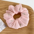 Dettaglio di elastico in chiffon rosa con ricamo floreale su un vassoio di legno - Fiore Rosa