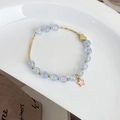 Detail eines hellblauen Perlenarmbands mit Herz- und Sternanhängern auf weißer Keramik - Blau