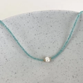 Detail view of a blue beaded necklace featuring a central pearl on a ceramic plate - Lake Blue Beads