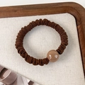 Detailed view of elastic brown scrunchie with round bead on textured linen tray - Coffee (24094A)