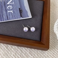 Gros plan de boucles d'oreilles perles irisées sur un présentoir gris minimaliste - Rose