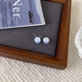 Gros plan de boucles d'oreilles perles bleues irisées sur un plateau de présentation en velours - Bleu