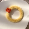 Close-up of a soft yellow plush hair tie with an orange suede label on white ceramic - Yellow
