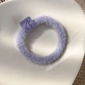 Close-up of light purple plush hair scrunchie with dolphin emblem on ceramic background - Purple