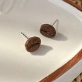 Macro close-up of realistic coffee bean earrings showing natural texture on a ceramic tray - Coffee Bean Style