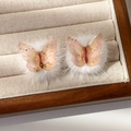 Vue détaillée de boucles d'oreilles papillon en résine avec feuille d'or et pompons blancs - Blanc