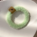 Close-up of a light green plush hair scrunchie with a brown leather shell logo tag - Green