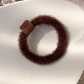 Close-up of fluffy brown plush hair tie with matte leather buckle on white ceramic plate - Dark Coffee