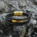 Multi-layer black leather braided bracelet with matte gold magnetic clasp on rock background - Gold Style