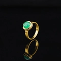 Elegant minimalist gold ring featuring a polished green gemstone on a dark reflective surface - Gold Band Green Gemstone
