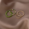 Close-up of four-piece ring set with colorful crystal beads and gold bands on brown silk - C Green / Green