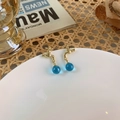 Detalle de pendientes de grifo dorado con bolas de cristal azul en plato blanco - Dorado