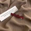 Macro detail of wave-shaped dark red resin hair clip on fabric and paper card - Red