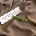 Detail of a wavy grass green matte hair clip on brown silk fabric with a metal base - Light Green