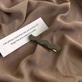 Detail view of wavy olive green matte hair clip on brown fabric with decorative card - Gray