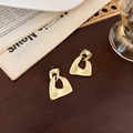 Detalle de los pendientes geométricos en oro mate sobre una superficie de madera oscura - Estilo Triángulo Geométrico Oro Mate (C 几何三角)