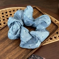 Close-up of light blue satin scrunchie with white floral patterns on a wooden tray - Blue
