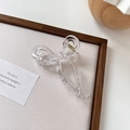 Detalle de una pinza para el pelo transparente con forma de lazo y resorte de metal dorado - Transparente