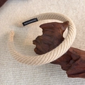 Nahaufnahme von beige gestricktem Schwamm-Stirnband mit Handmade-Label auf Holz - Beige Zopfmuster (26004B)
