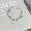 Detail of beaded bracelet with moon and key charms on a minimalist grey background - Green