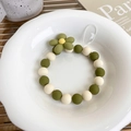 Dettaglio del cinturino per cellulare in perline verde oliva con ciondolo a fiore su piatto - Stile Fiore Verde e Bianco Opaco