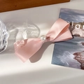 Detalle de horquilla con lazo de satén rosa y perla central bajo luz suave - Rosa