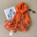 Detailed flat lay of orange floral chiffon scarf with sunglasses and brand tag - Orange Floral Style