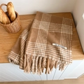 Close-up of a brown plaid scarf featuring thick tassels and a soft textured fabric detail - Camel