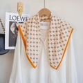 Detail van beige bloemensjaal met oranje bies gedrapeerd op een wit overhemd - Oranje