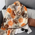 Détail d'une écharpe à fleurs orange et marron sur un cintre en bois dans un décor cosy - Orange