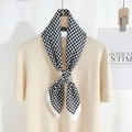 Detailed view of a black and white houndstooth silk scarf tied on a beige sweater - White Edge Pink